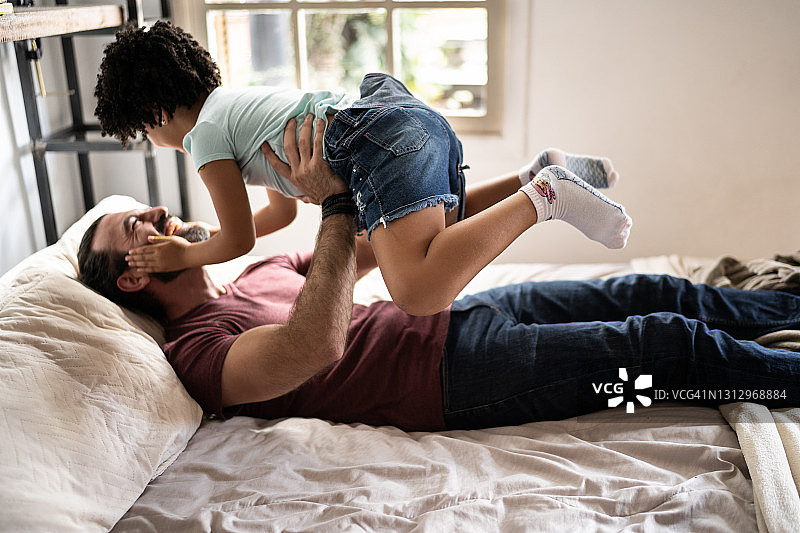 父亲在家中床上和女儿玩耍，将她举起来图片素材