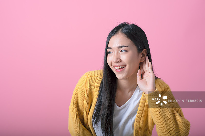 在粉色墙壁前倾听秘密的年轻漂亮金发女子图片素材