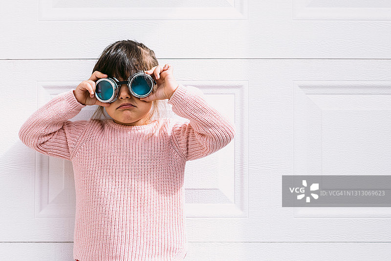 在白色车库门前，戴着维多利亚眼镜的黑发粉色毛衣小女孩图片素材