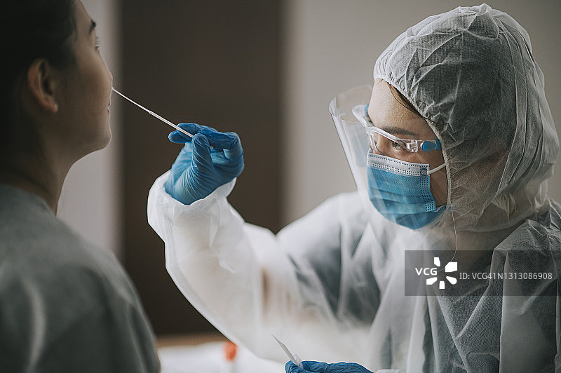戴着个人防护装备的亚洲华人女医生为患者进行新冠病毒鼻拭子检测。图片素材