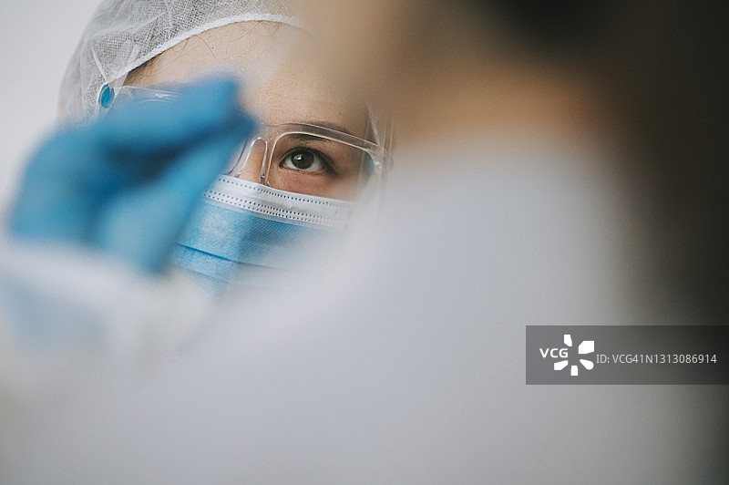 戴着个人防护装备的亚洲华人女医生为患者进行新冠病毒鼻拭子检测。图片素材