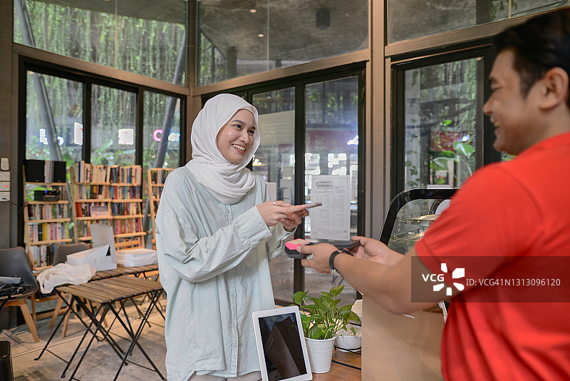 戴着头巾的年轻女人使用非现金支付设备付款图片素材