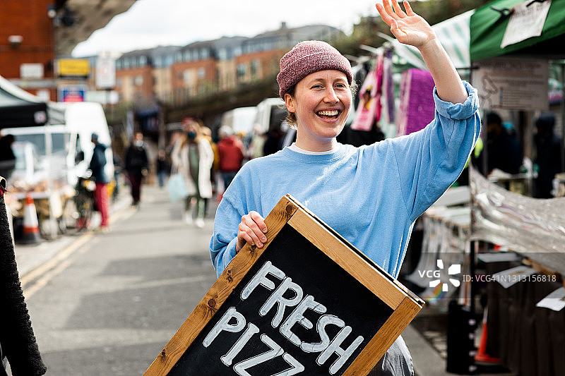 在户外市场手举新鲜披萨招牌的年轻人图片素材