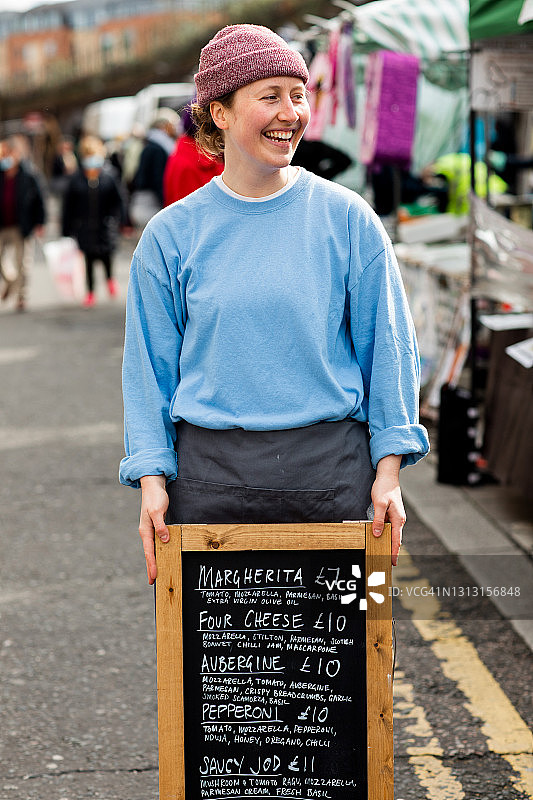 在户外市场手举新鲜披萨招牌的年轻人图片素材