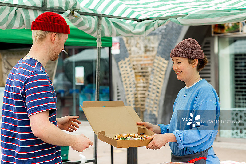 一位年轻人在户外市场的披萨摊位为顾客服务图片素材