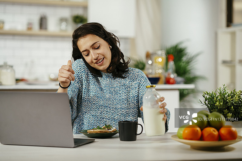 美丽的女人一边吃三明治一边进行视频通话图片素材