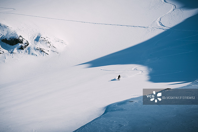 滑雪者从覆盖着冰雪的冰川上滑下，穿过引人注目的阴影图片素材