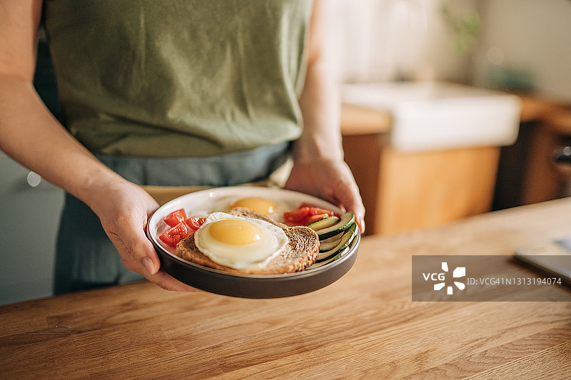 女孩在煎锅上方放入三个鸡蛋，配以香草、奶酪和西红柿，制作早餐图片素材