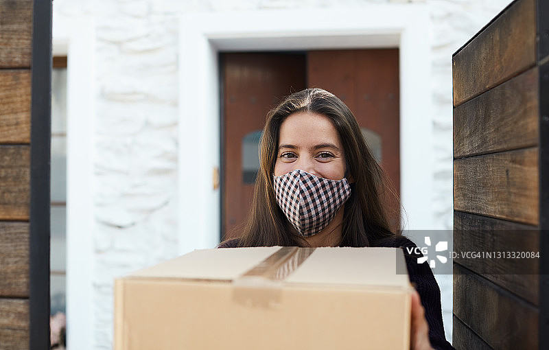 戴着防护COVID-19口罩微笑地接收包裹图片素材