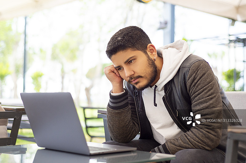 坐在咖啡店里情绪低落地看着电脑屏幕的年轻男人图片素材