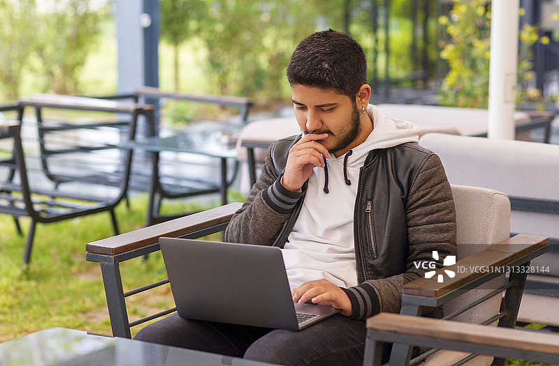 年轻男人在咖啡馆工作，手捂嘴巴，情绪紧张图片素材