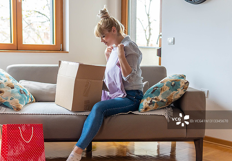 快乐的年轻女子在家中沙发上打开网购订单纸箱图片素材