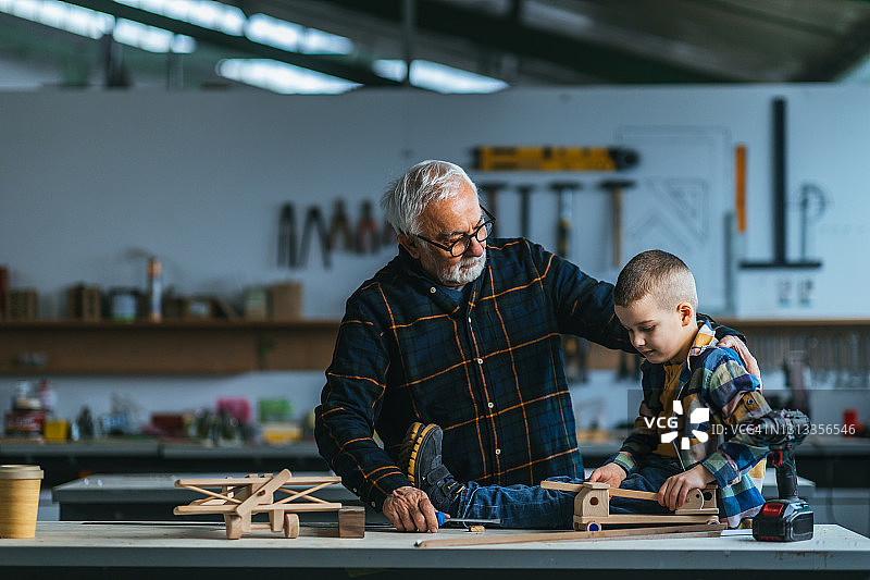 男孩和他的祖父在木工车间玩木制玩具图片素材