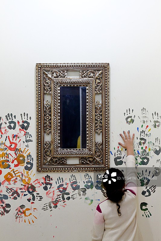在银镜周围墙上进行彩色手印绘画的年轻女孩图片素材