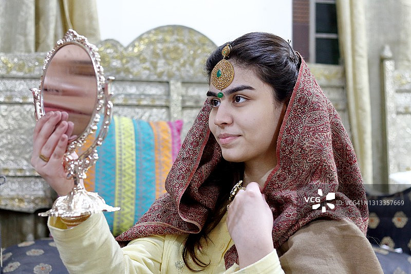 戴着头饰，在梳妆镜中看自己的年轻女子侧视图图片素材