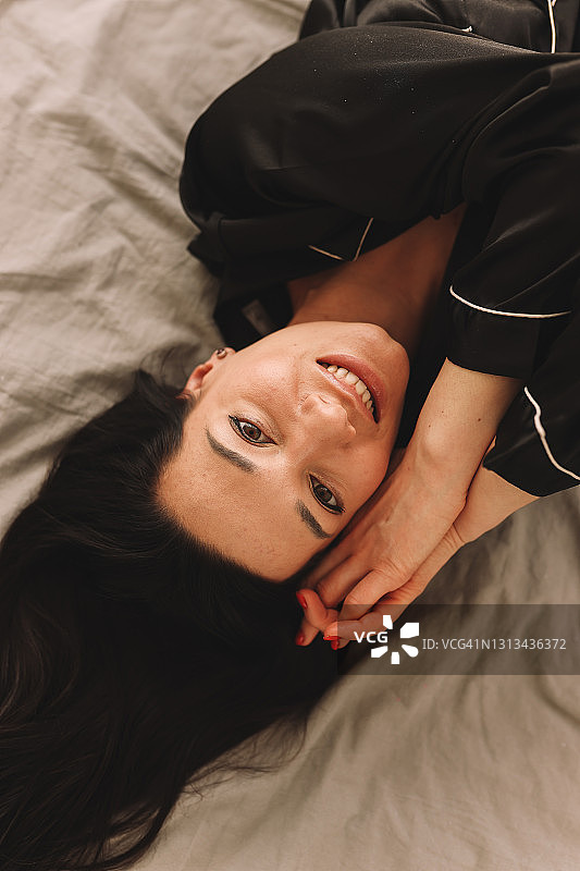 穿着黑色家居服的快乐年轻女子在卧室的床上休息图片素材