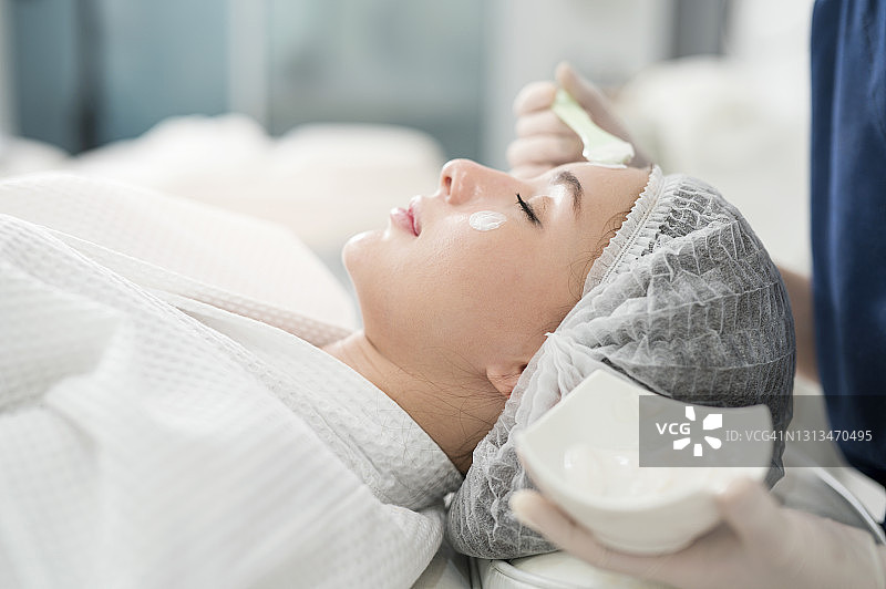 年轻女子在美容诊所接受面部护理，护士正在为其进行面部去角质护理。 皮肤护理诊所业务图片素材