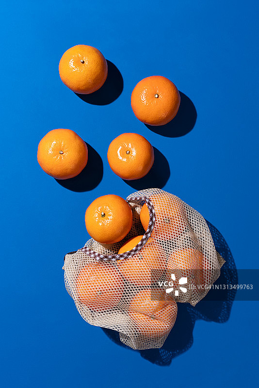 蓝色背景上的可重复使用网袋中的橘子图片素材
