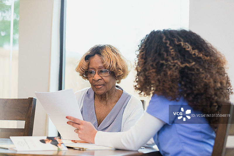 年长的女人在听着，一位无法辨认的护士协助她处理文书工作图片素材