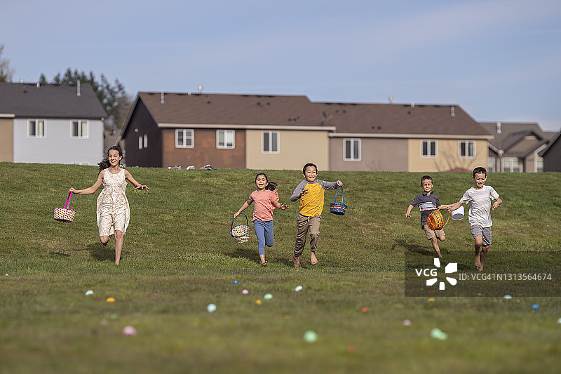 不同种族的孩子们在复活节彩蛋游戏中跑下草坡图片素材