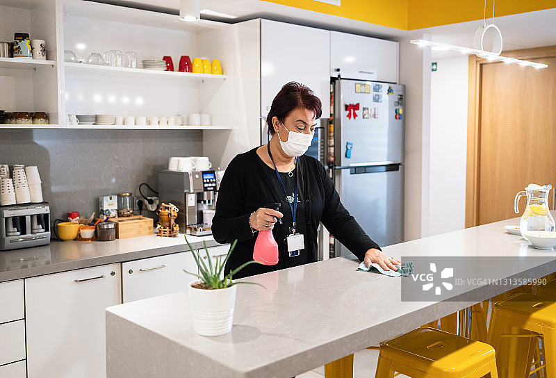 戴着防护口罩消毒办公室厨房的女人图片素材