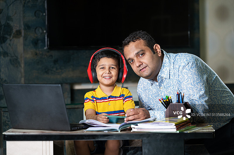 快乐的父亲在家用笔记本电脑和智能手机帮助儿子学习图片素材