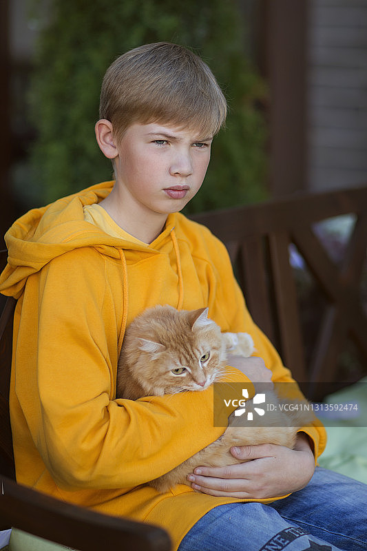 少女坐在户外长椅上，怀里抱着一只红猫——库存照片图片素材