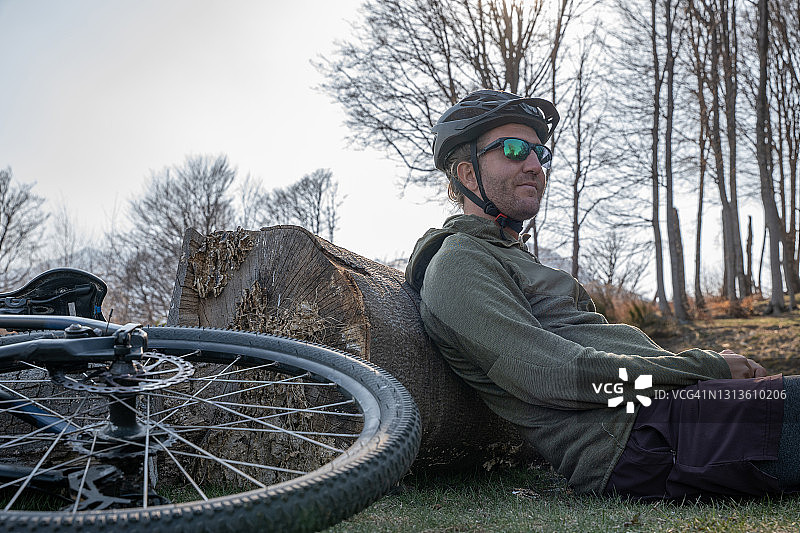 男子山地自行车手坐在树干上休息图片素材
