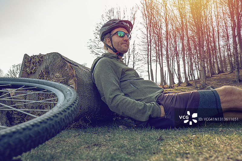 男子山地自行车手坐在树干上休息图片素材