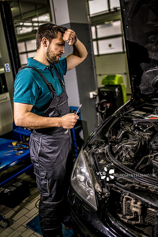 汽车修理店里检查发动机问题的担忧的技工图片素材