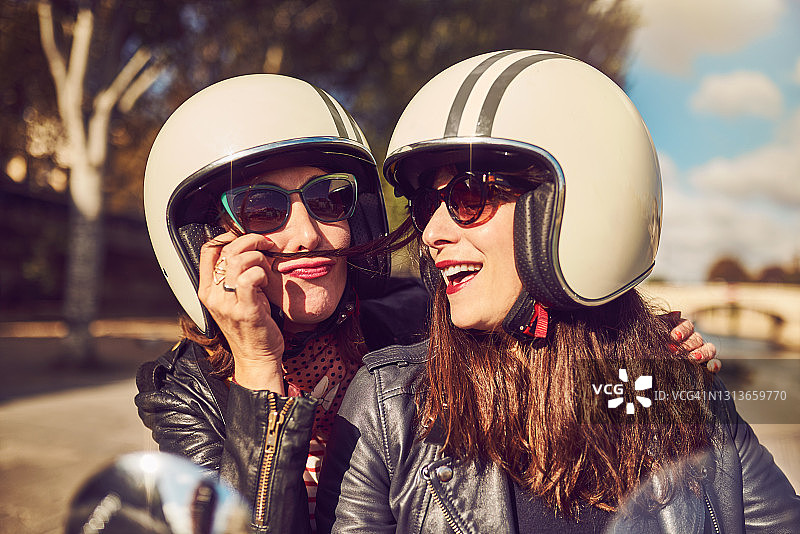 两位无忧无虑的年轻女子白天骑着红色滑板车在城市里游玩图片素材