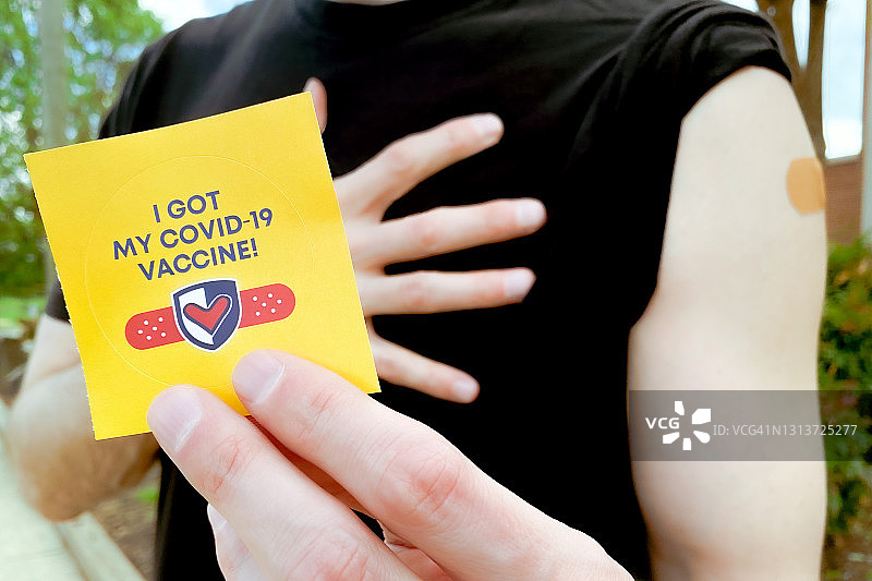 接种新冠疫苗后手臂上贴着胶布并拿着贴纸的男人图片素材