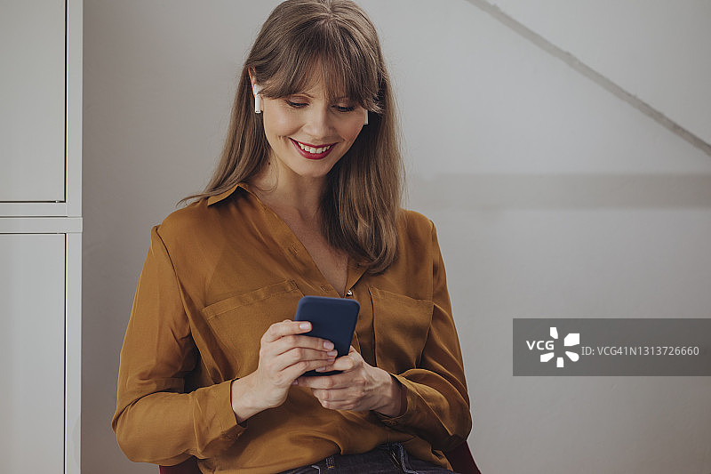 快乐的金发女商人戴着耳机，在手机上看东西图片素材