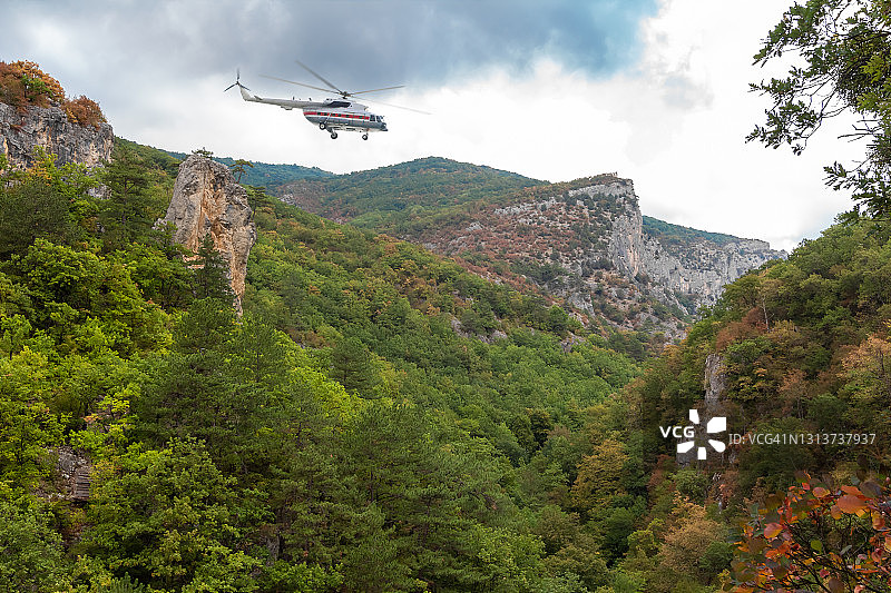 救援直升机在多云阴雨天气中飞越山谷和森林地区图片素材