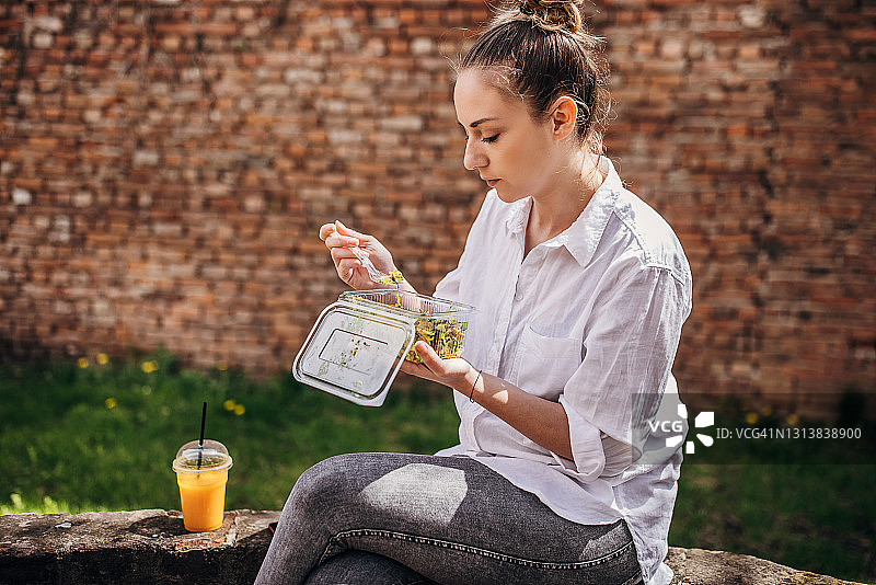 在公园里吃健康沙拉的年轻女人图片素材