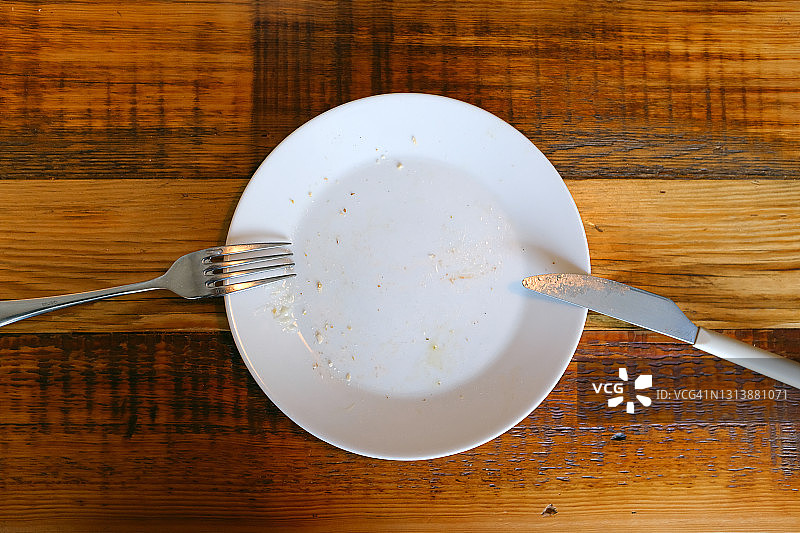 脏盘子上的餐具，木质背景，咖啡馆或餐厅的餐桌，午餐/晚餐/早餐结束，白色盘子上的刀叉，文案空间图片素材