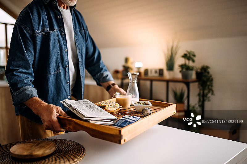 年长的男人在这个舒适的公寓里用托盘端茶图片素材