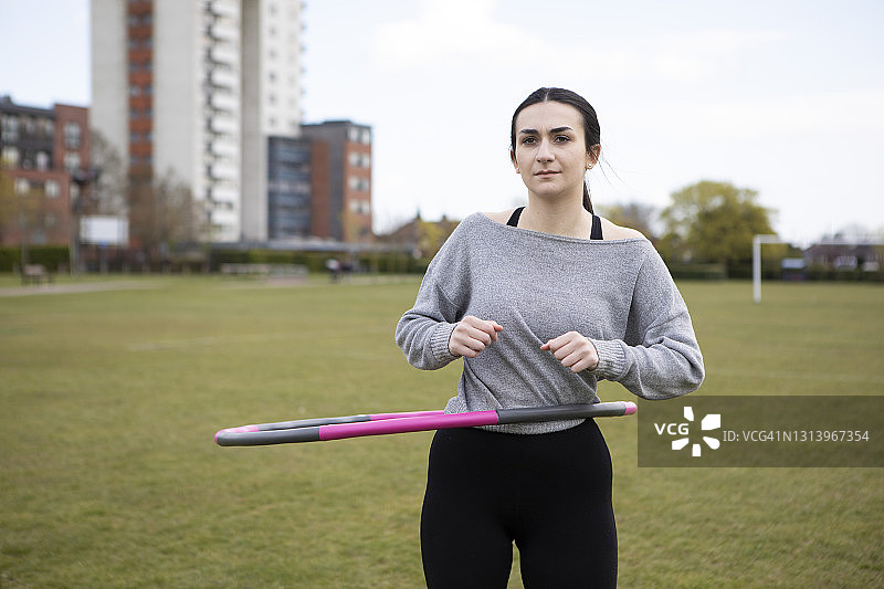年轻女子在公园里玩呼啦圈，远处是住房和塔楼图片素材