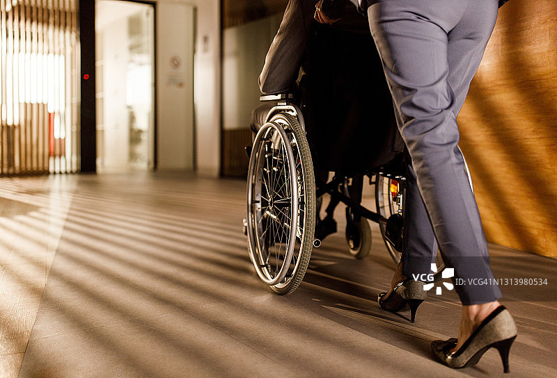 一位无法辨认的女商人帮助坐在轮椅上的同事图片素材