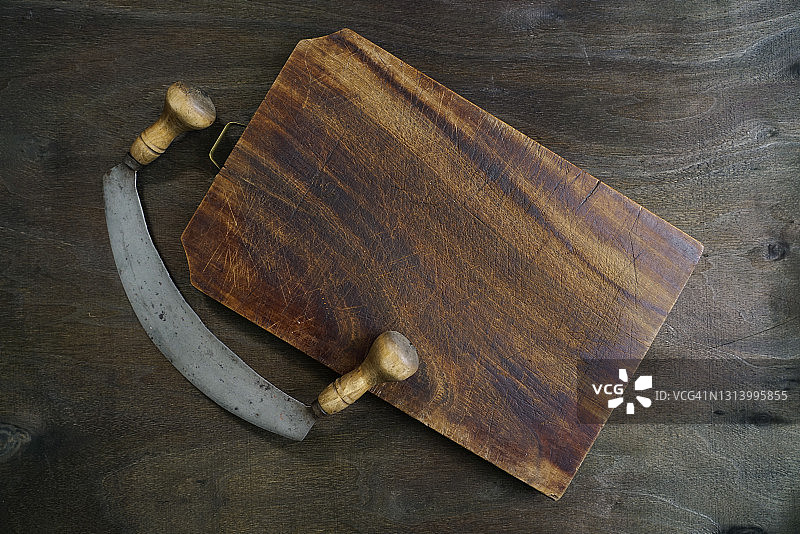 深色木质背景上的旧式厨房弯月刀和木质砧板，带复制空间。意大利。欧洲图片素材
