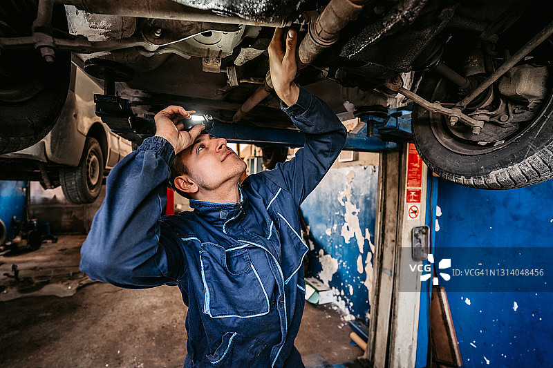 汽车修理工在车间用灯检查汽车图片素材