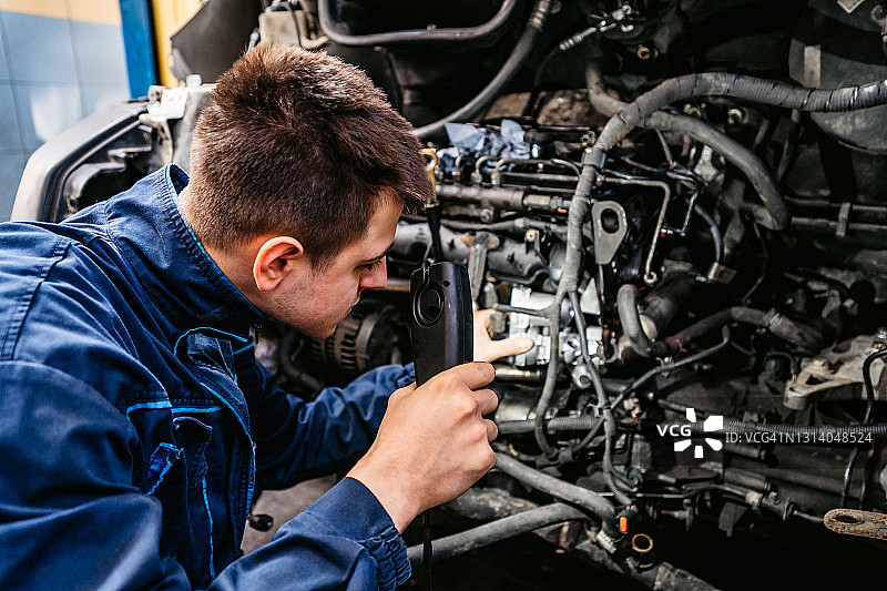 汽车修理工在车间用灯检查汽车图片素材