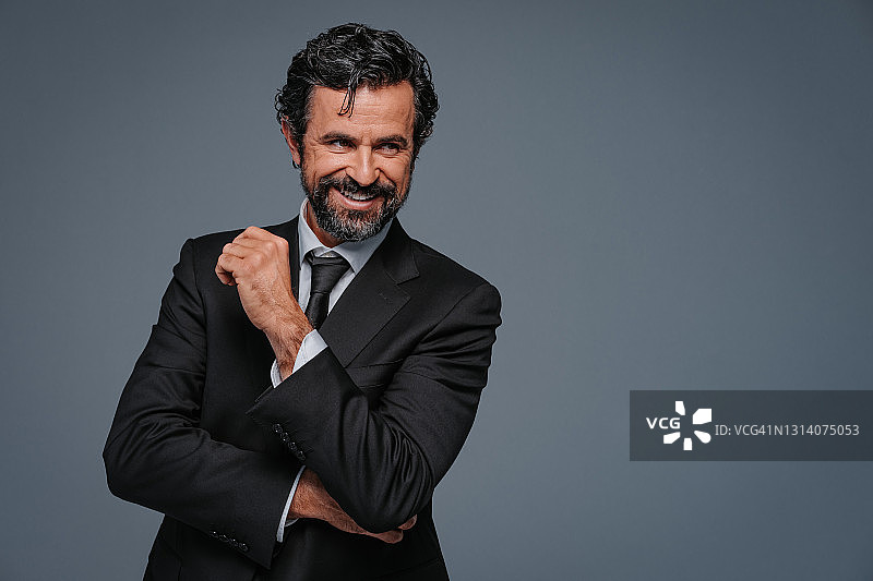 非常英俊的微笑商务男士的放松姿势工作室肖像，拥有自然的黑色和灰色头发及胡须图片素材