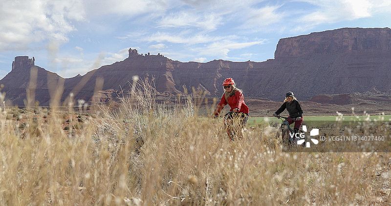 骑山地自行车的女人们穿过草地图片素材