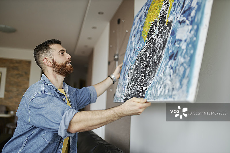 在客厅墙上挂画的络腮胡男人图片素材