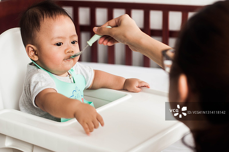 东南亚母亲用蔬菜泥喂她的男婴图片素材