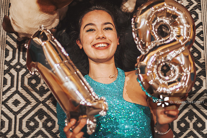 拉丁裔少女在生日派对上拿着18岁金色气球躺在地毯上的肖像图片素材