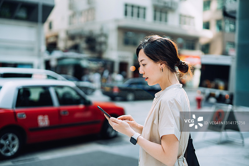年轻的亚洲女性在城市街道上用手机App叫出租车图片素材