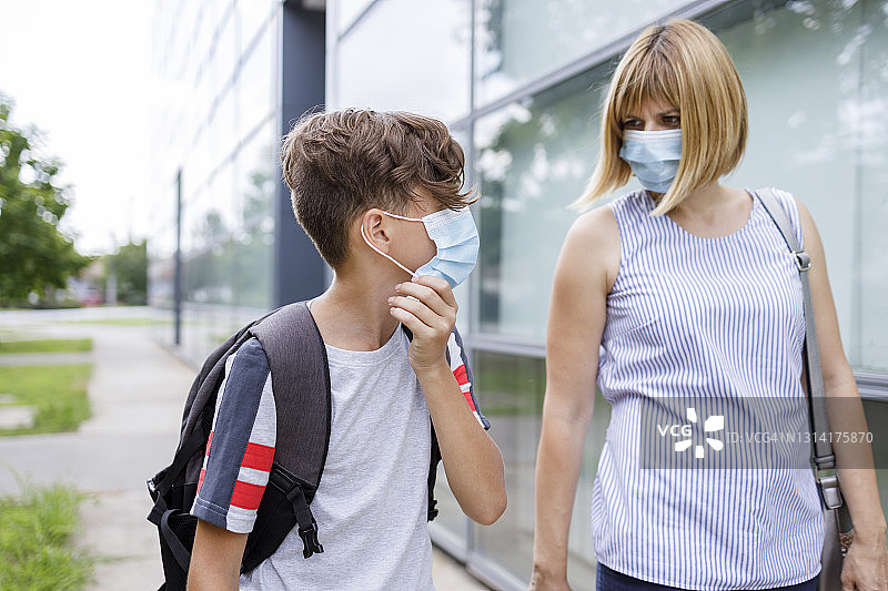 一名女子走在街上，旁边是一名戴着口罩的男学生图片素材