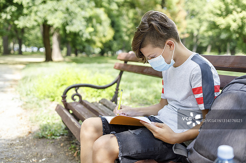 戴着口罩在公园里做作业的男孩图片素材
